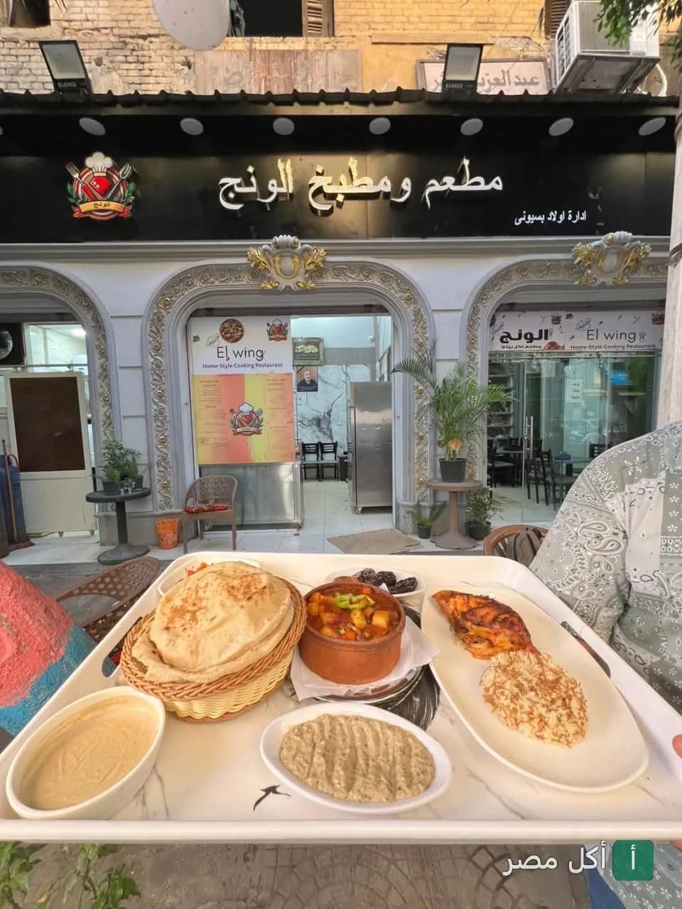 صينية أكل مصري من مطعم ومطبخ الونج في عابدين تتضمن طاجن وخضار وعيش بلدي أمام واجهة المطعم.