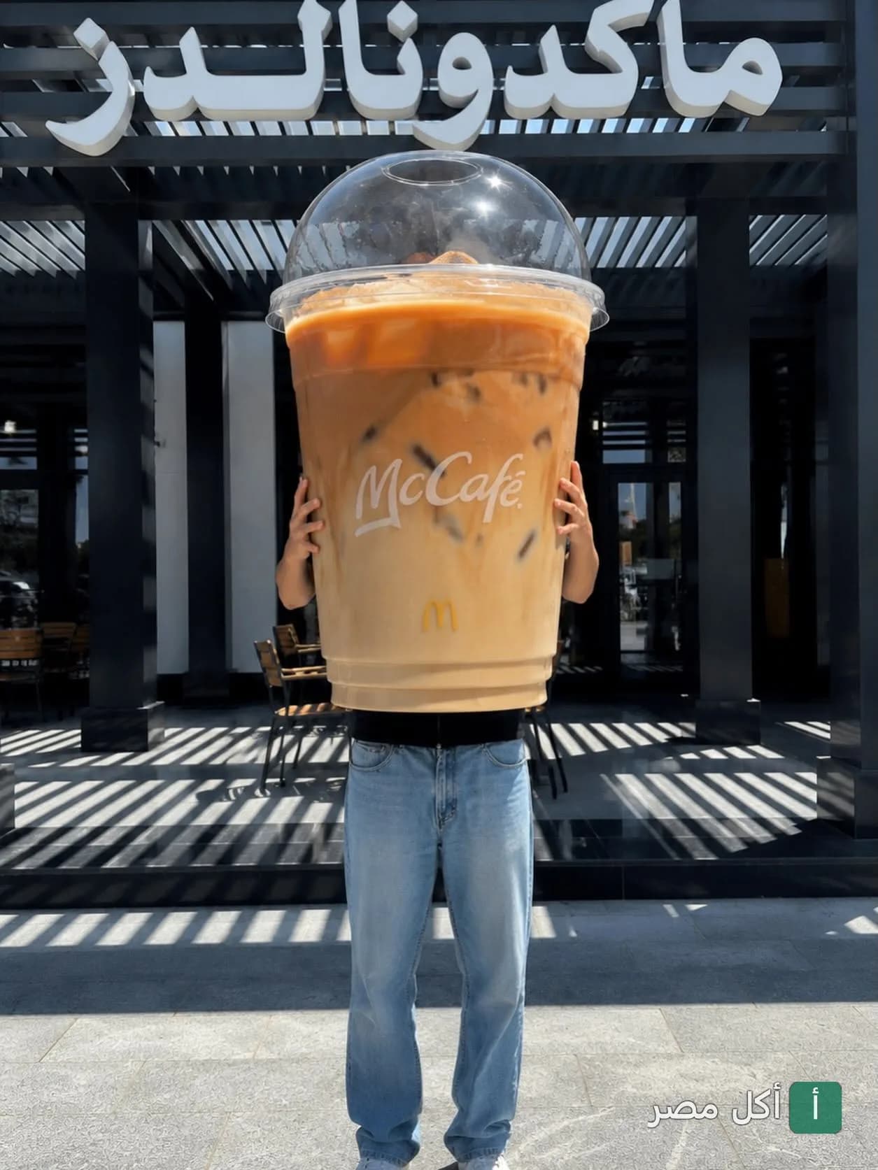 شخص يحمل كوب قهوة مثلجة ضخم من ماك كافيه أمام فرع ماكدونالدز في عابدين.