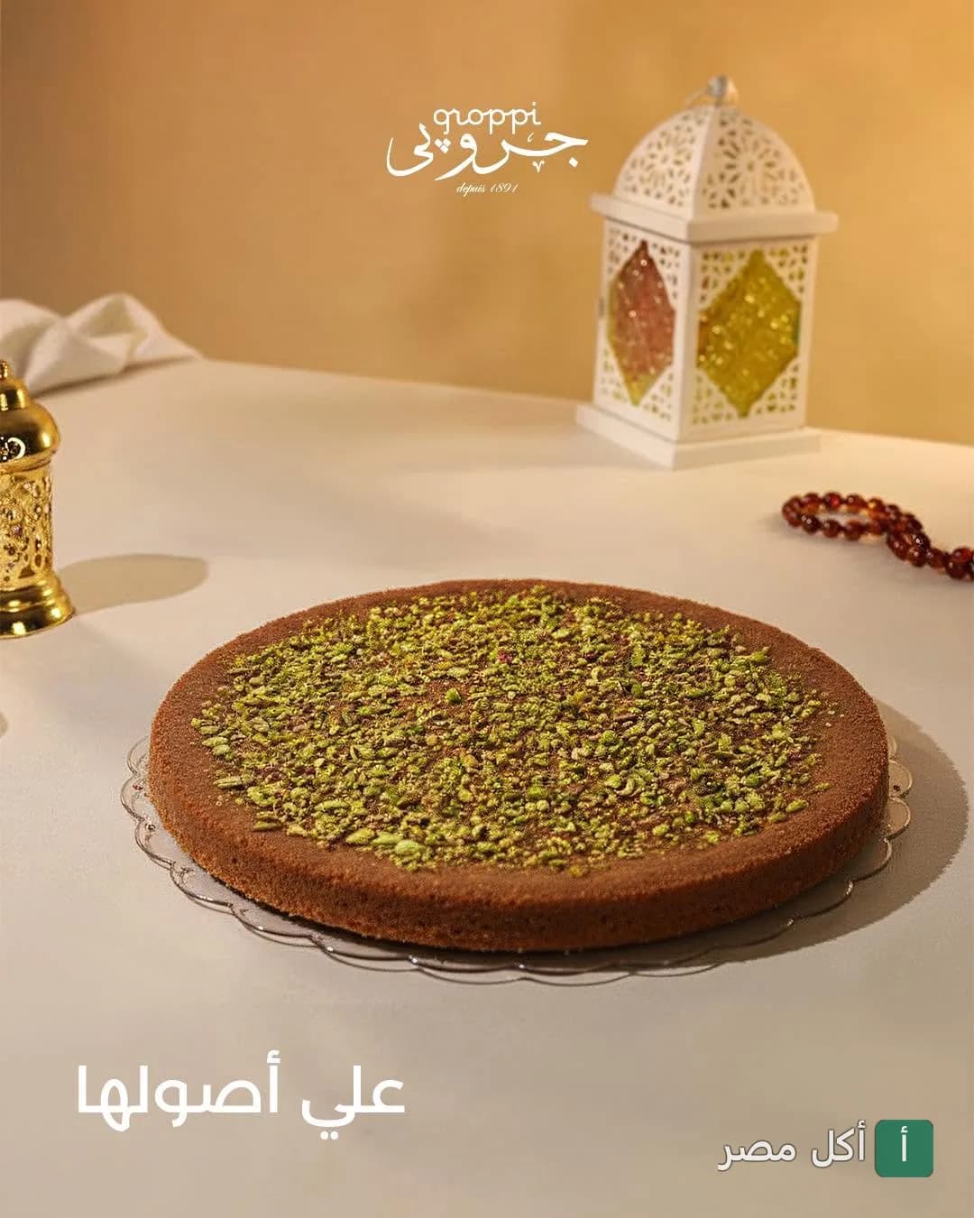 طبق كنافة مزين بالفستق من جروبي طلعت حرب مع فانوس رمضان في الخلفية.