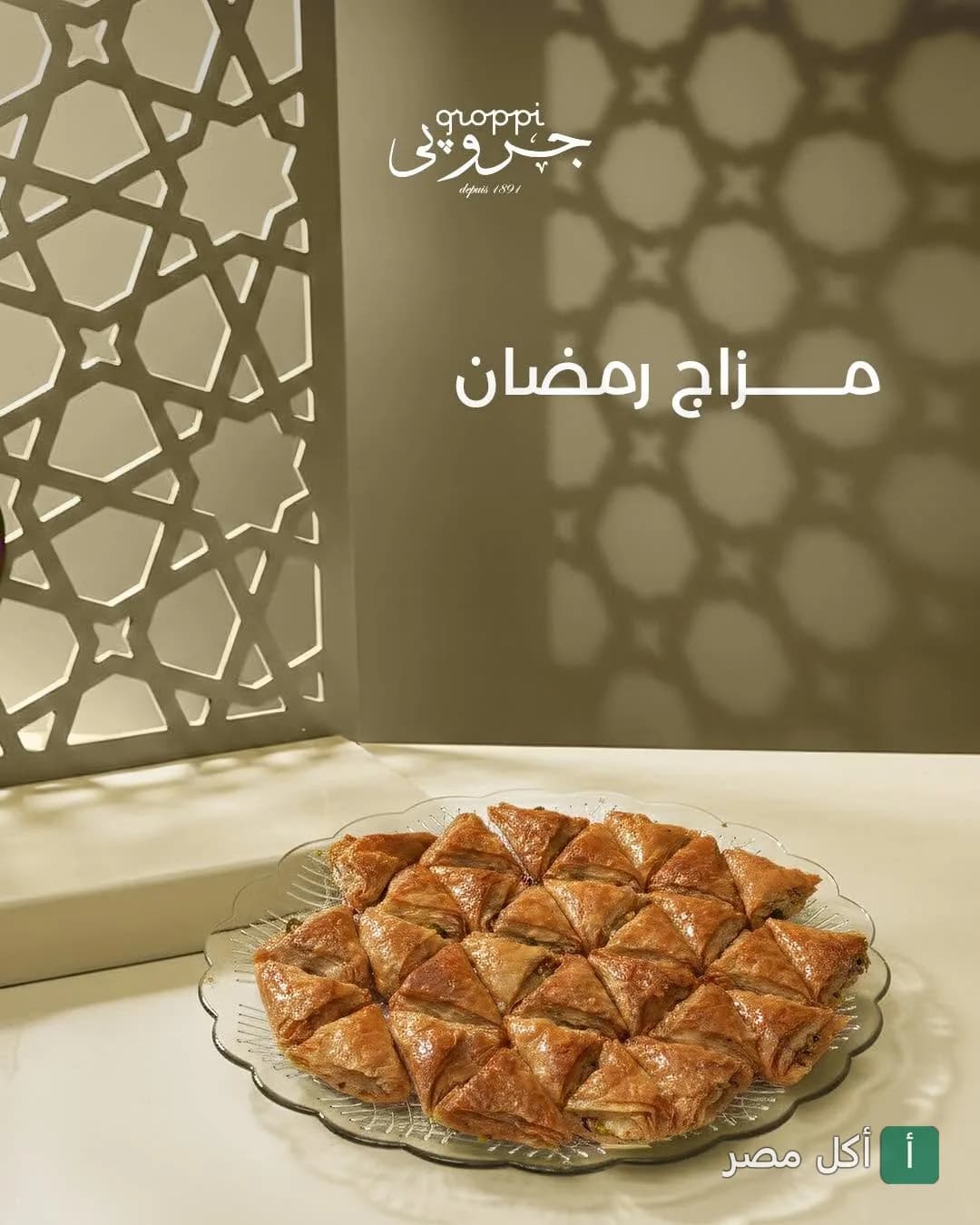 طبق بقلاوة مثلثات من جروبى طلعت حرب مع خلفية بنقوش إسلامية.