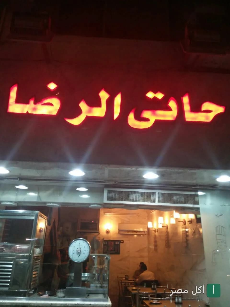 واجهة مطعم حاتي الرضا في عين شمس مع لافتة مضيئة باللون الأحمر.