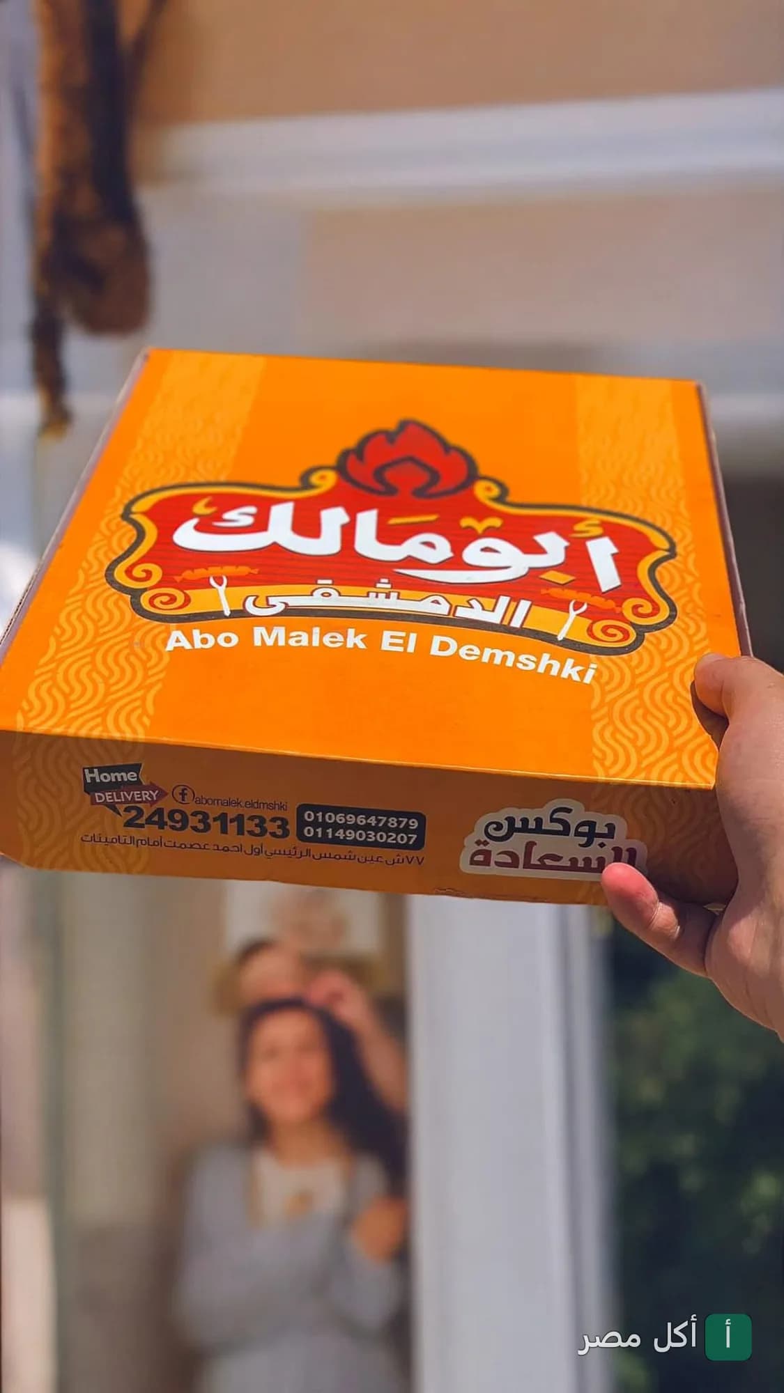 يد تحمل علبة وجبة من مطعم أبو مالك الدمشقي في عين شمس.