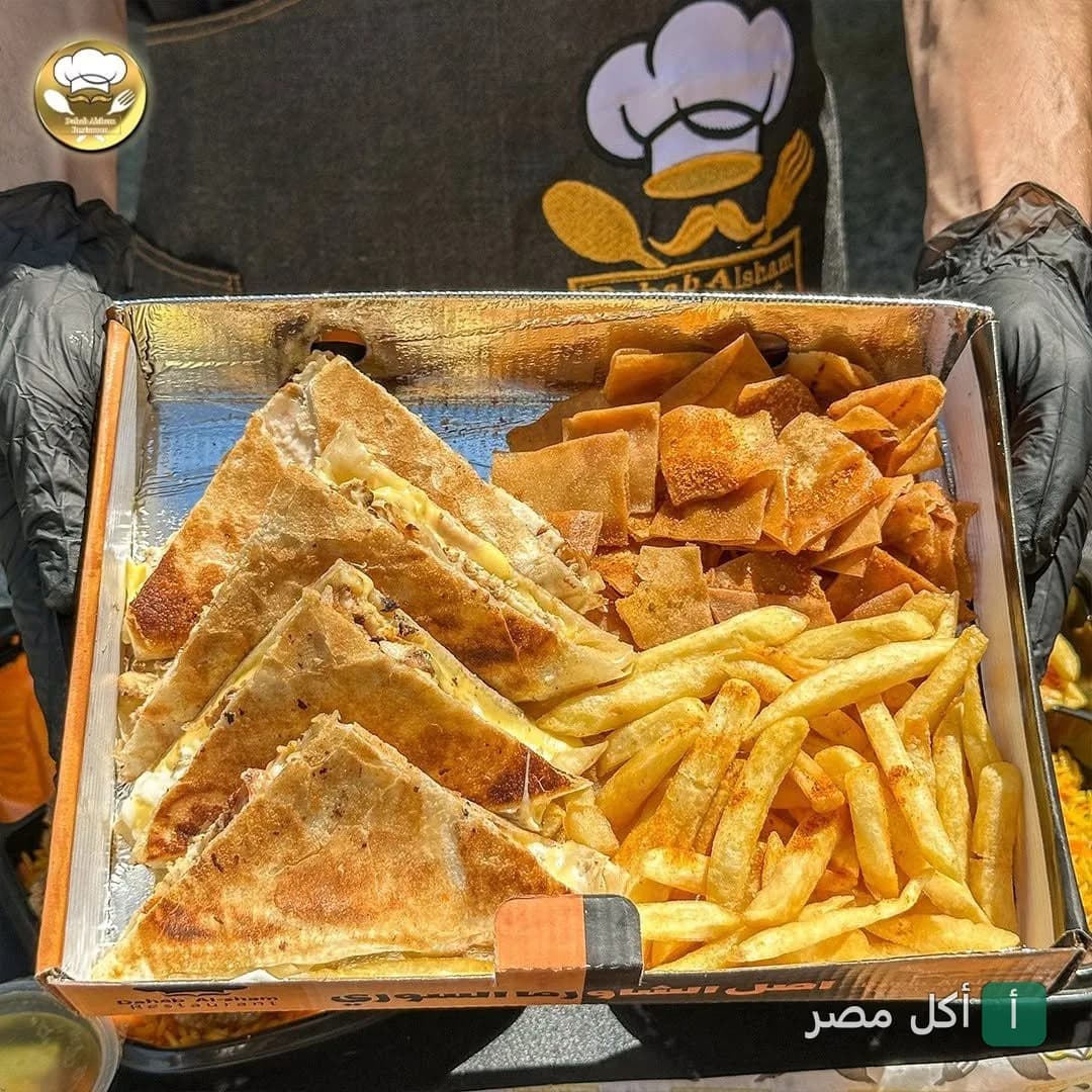صندوق وجبة من مطعم دهب الشام في عين شمس يحتوي على ساندوتشات مقطعة مثلثات مع بطاطس مقلية وخبز محمص.