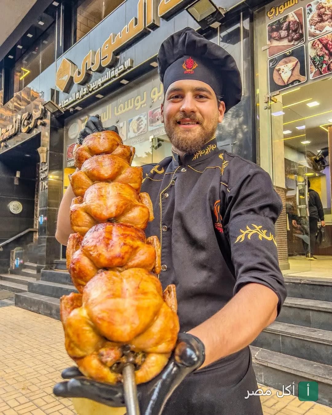 شيف مطعم أبو يوسف في عين شمس يحمل سيخ دجاج مشوي أمام واجهة المطعم.