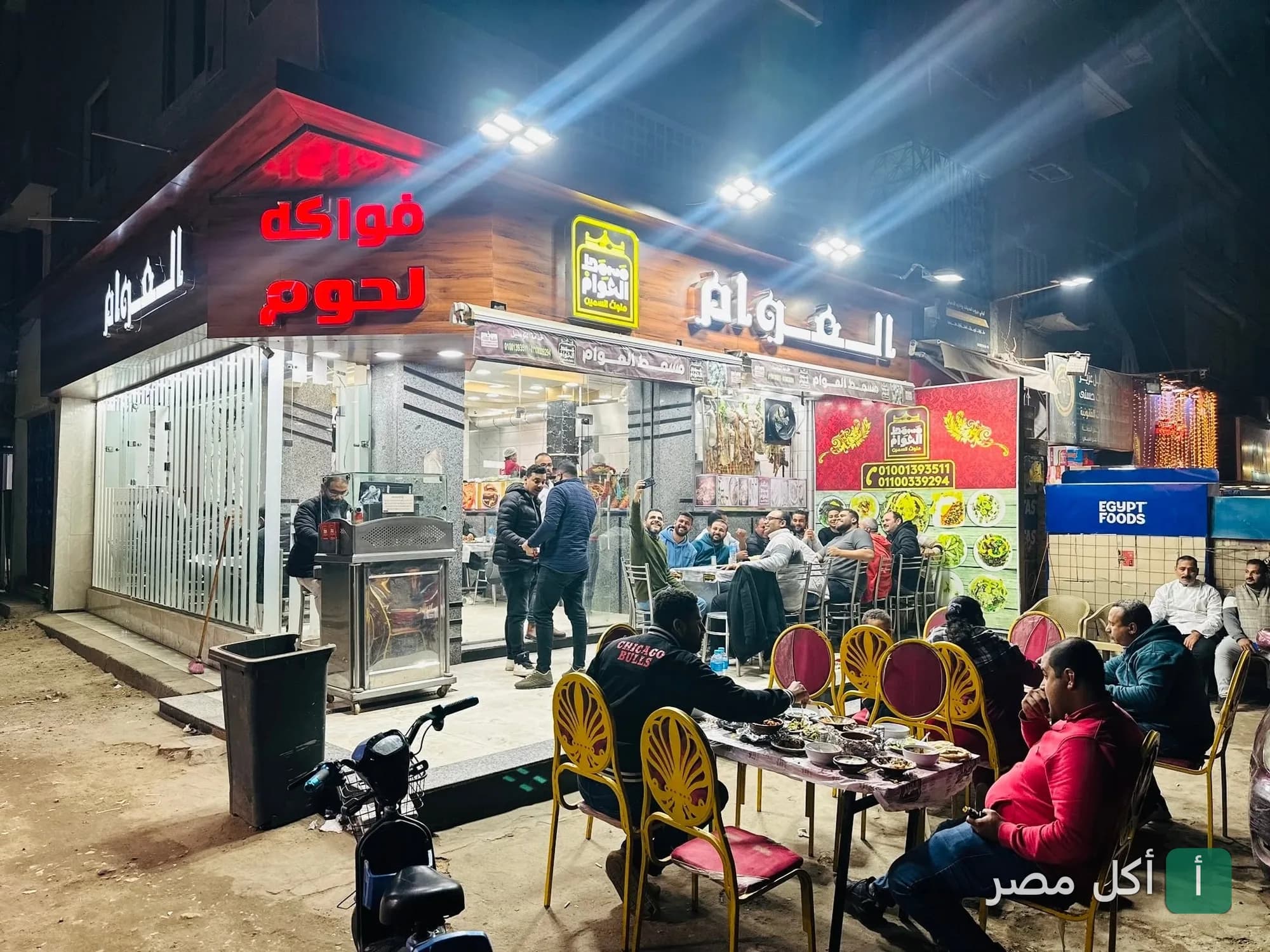 واجهة مسمط العوام في عين شمس ليلاً مع زبائن يجلسون في منطقة الطعام الخارجية.