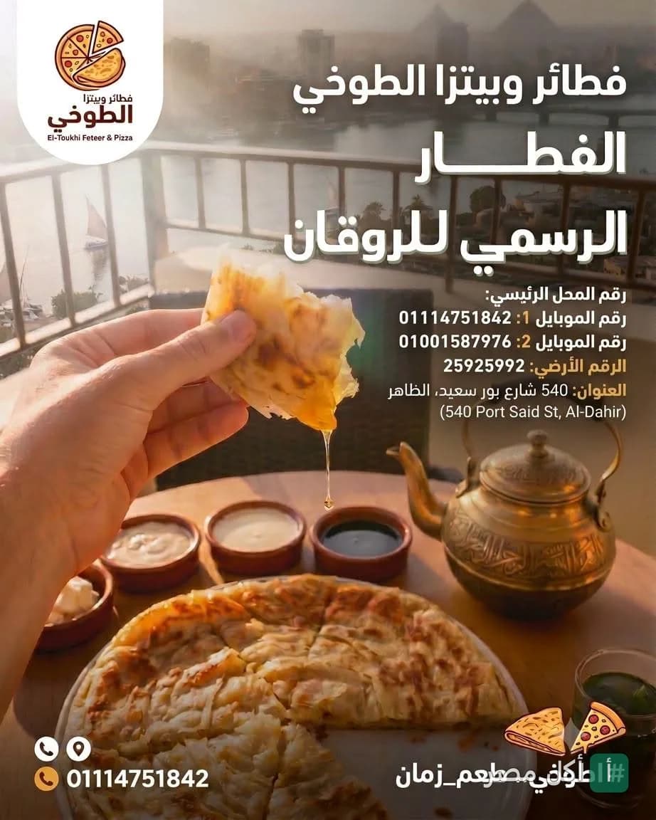 يد تمسك قطعة فطير مشلتت مع عسل في مطعم الطوخي، مع وجود فطيرة كاملة وأطباق جانبية وشاي على الطاولة.