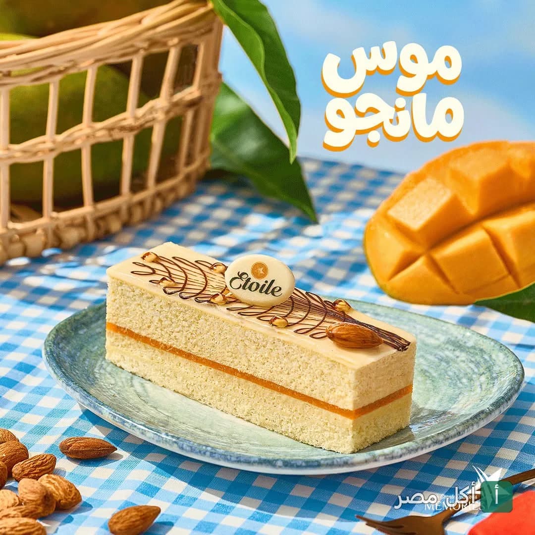 قطعة جاتوه موس المانجو من إيتوال، مزينة باللوز على طبق أزرق مع مانجو طازجة في الخلفية.