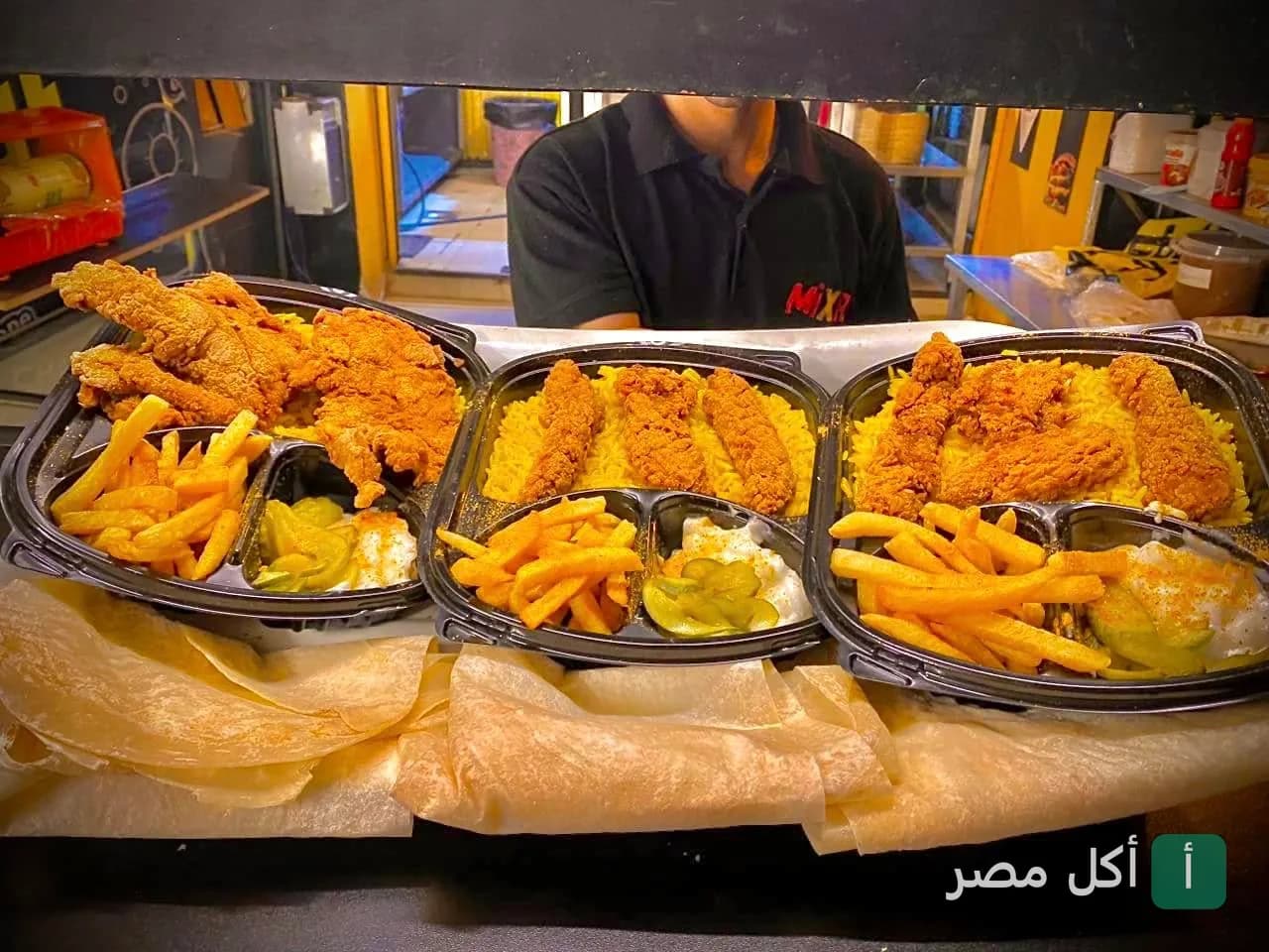 ثلاثة أطباق تحتوي على قطع دجاج مقرمشة مع أرز أصفر وبطاطس محمرة ومخلل في مطعم ميكسات كريب بعين شمس.