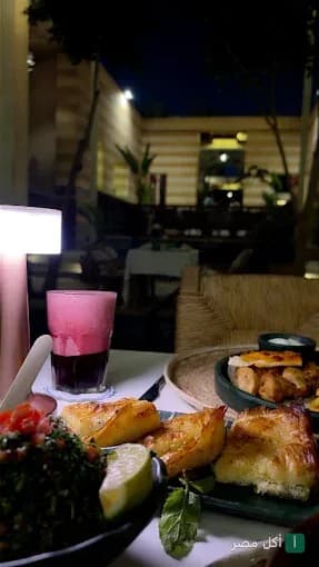 طاولة طعام في مطعم جرانيتا بالأزهر، تظهر أطباق مقبلات ومشروب أحمر في أجواء مسائية راقية.