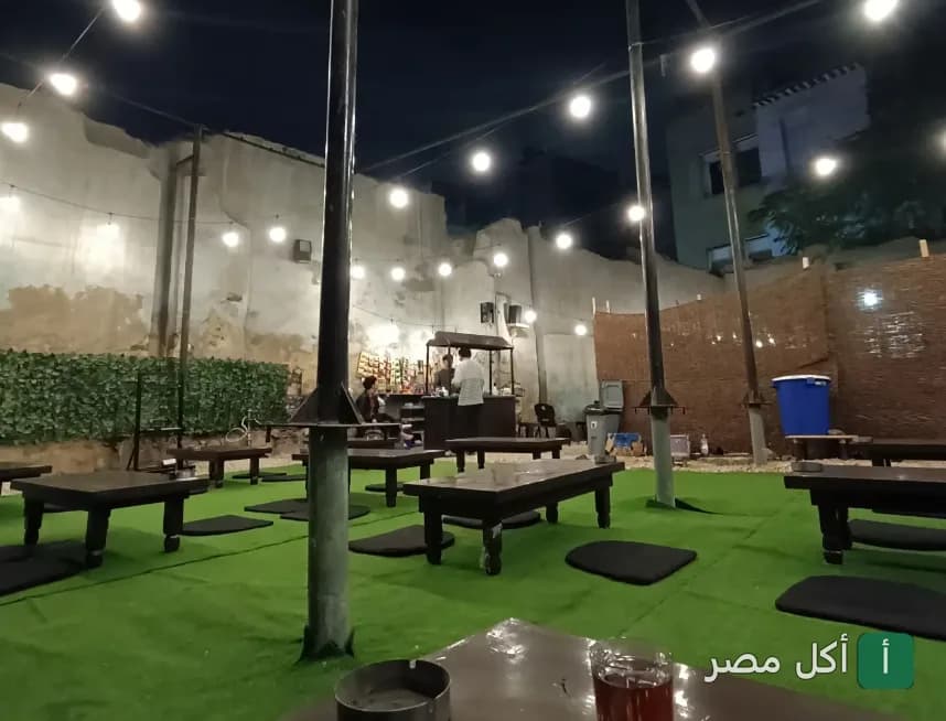 جلسات خارجية في مقهى أنتارا بالدرب الأحمر مع إضاءة دافئة وأرضية عشبية في المساء.