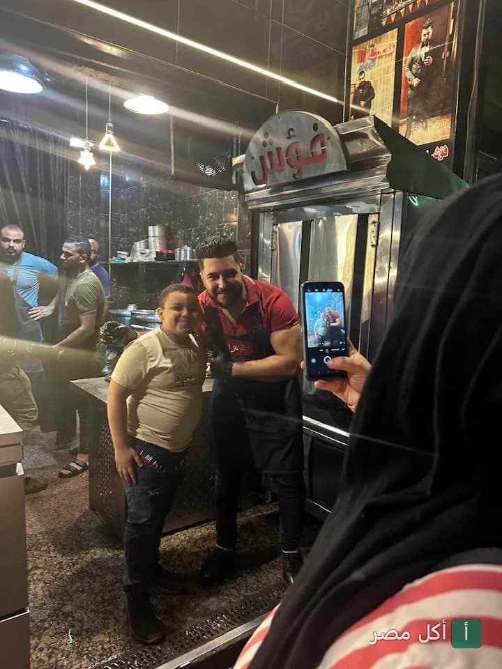 شيف مطعم فؤش ابن سيد في حوش قدم يلتقط صورة تذكارية مع أحد الزبائن أمام شواية المطعم.