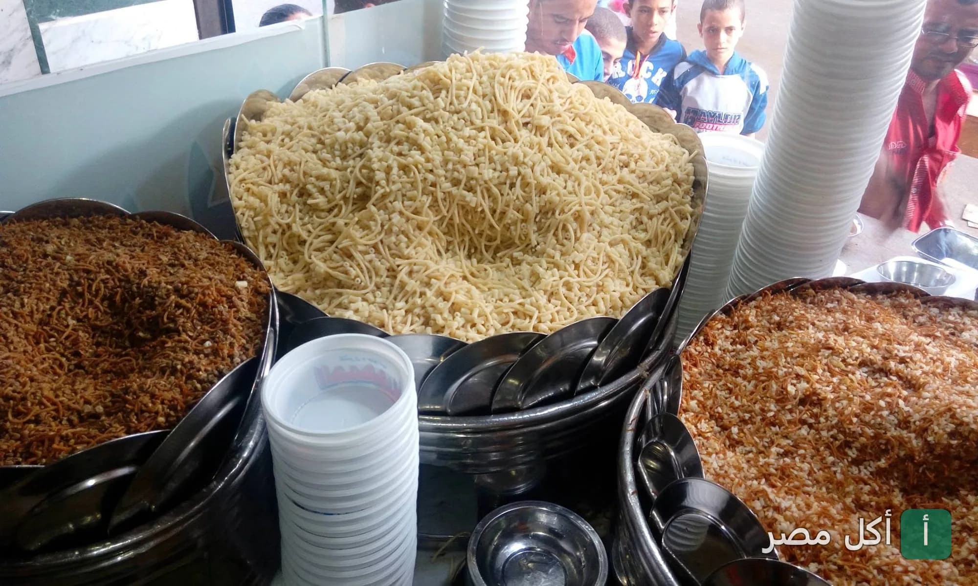 أطباق كبيرة مليئة بالمكرونة والأرز والبصل المقلي في مطعم كشري الجمهورية بالأزهر.