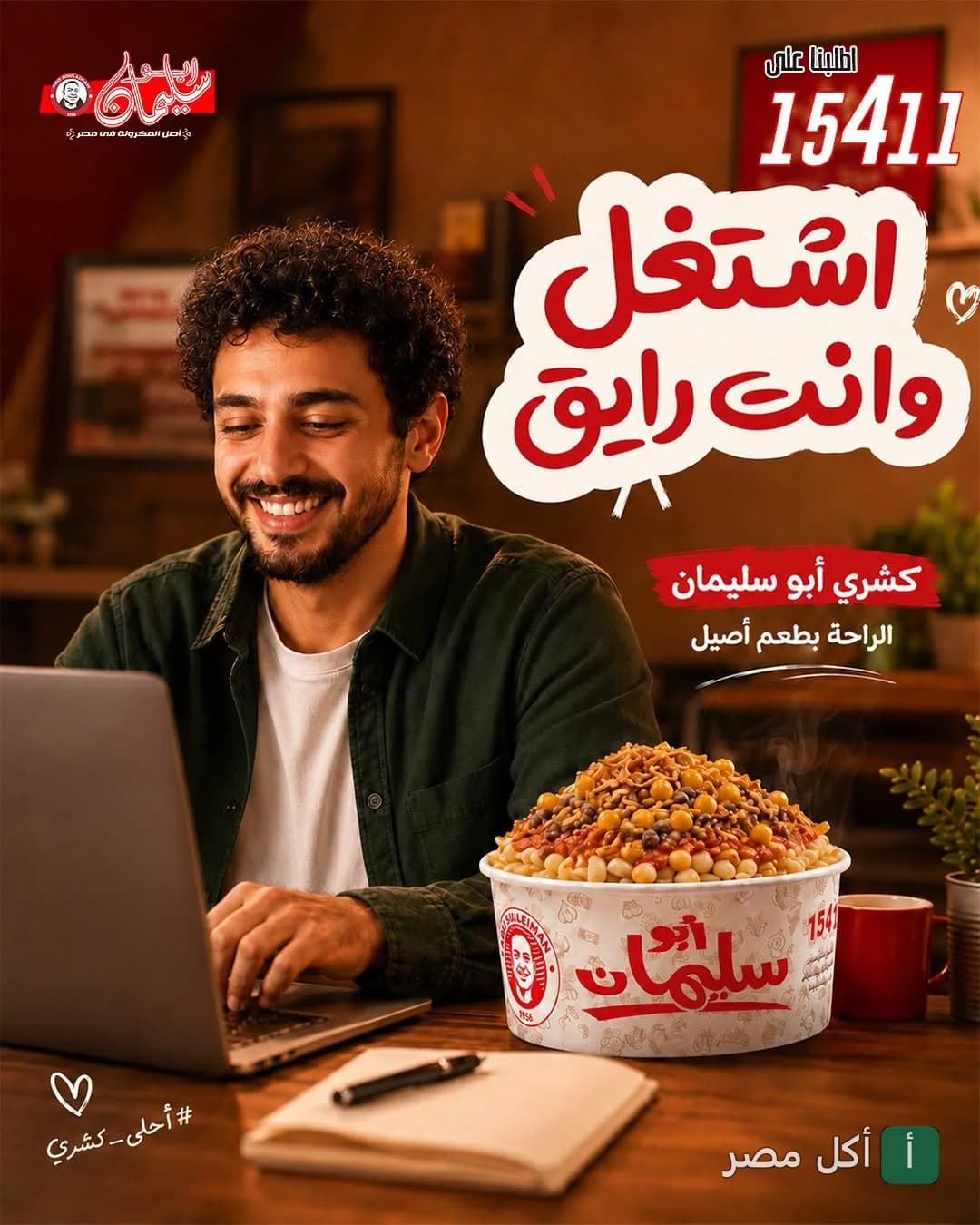 شاب يبتسم أثناء العمل على اللابتوب بجانبه علبة كشري من مطعم أبو سليمان للمكرونة.
