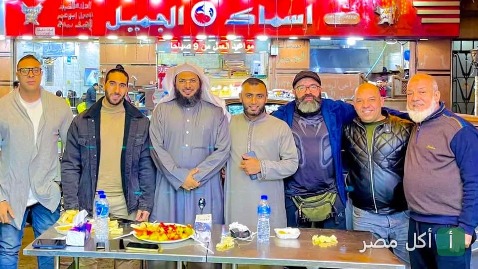 مجموعة من الأشخاص يقفون أمام واجهة مطعم اسماك الجميل في الخليفة.