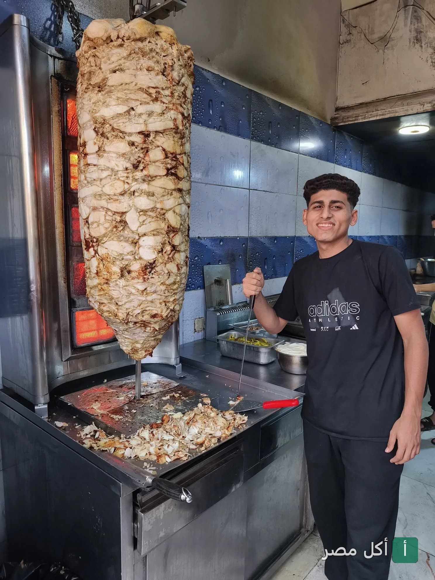 شيف يقطع شاورما دجاج طازجة على السيخ في مطعم نور الشام بالخليفة.