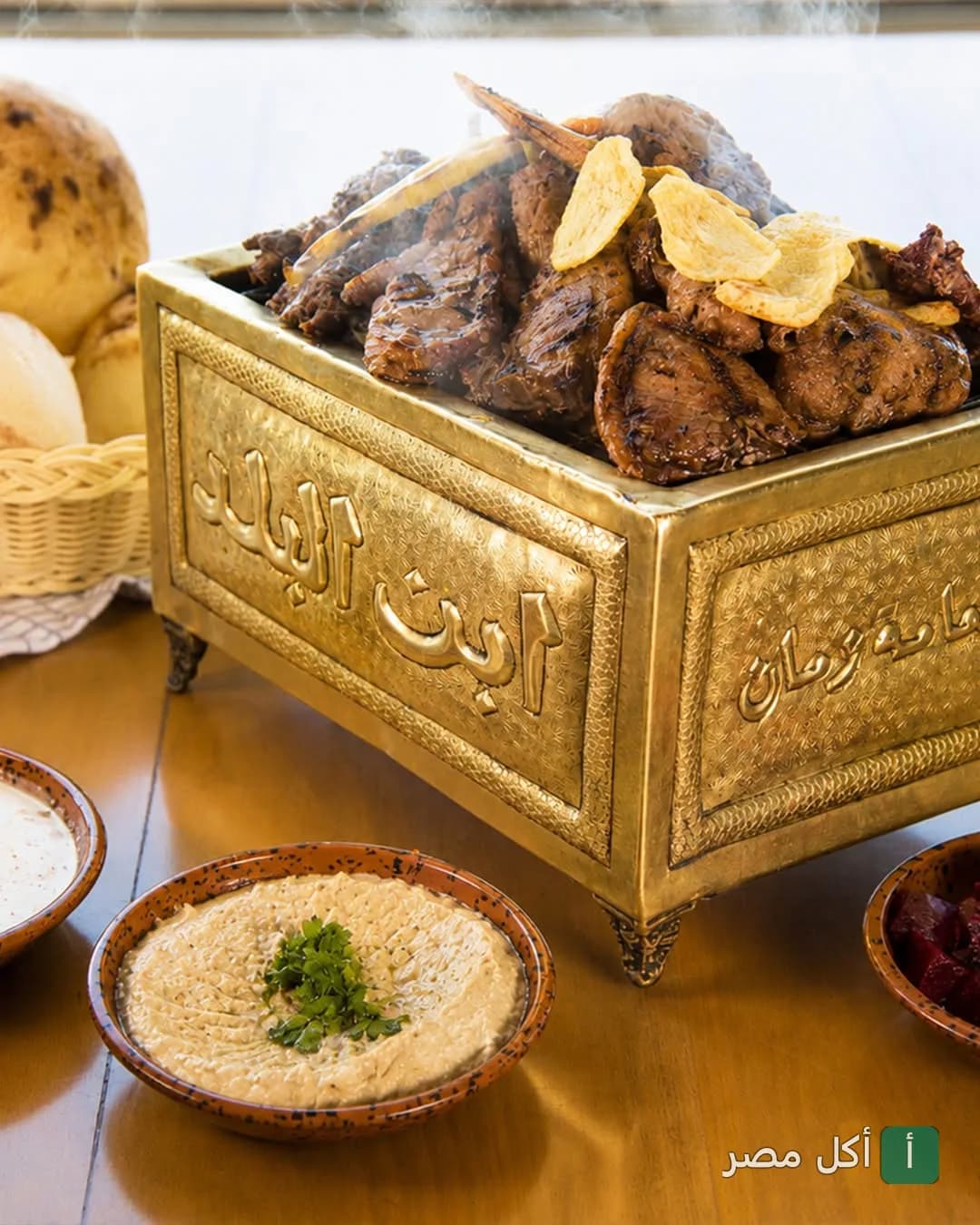 مشاوي مشكلة ساخنة تقدم في وعاء نحاسي تقليدي منقوش عليه اسم مطعم إبن البلد مع أطباق جانبية من المقبلات.