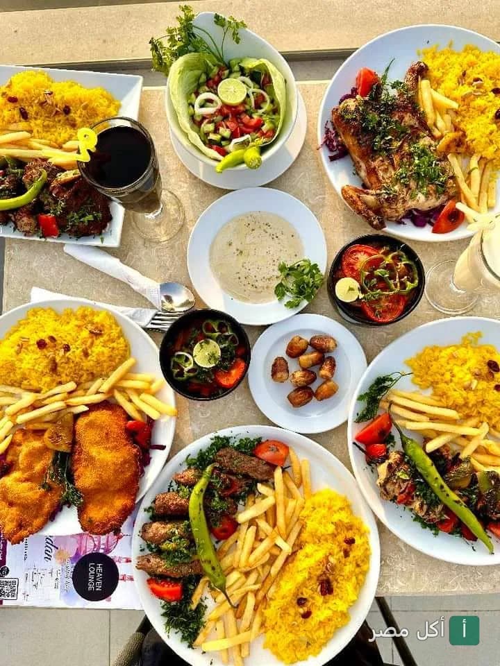 مائدة طعام متنوعة من هيفين لاونج آند روف توب فيو بنزلة السمان، تضم أطباق مشويات وأرز أصفر ومقبلات.