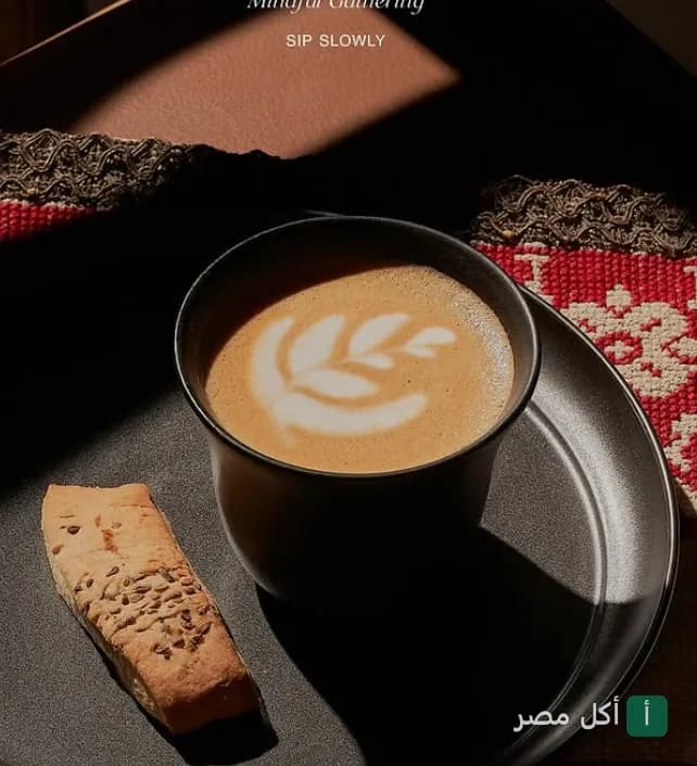 كوب قهوة لاتيه برسمة قلب على صينية سوداء مع قطعة بسكويت في مطعم بيت الشاي بالمنتزه.