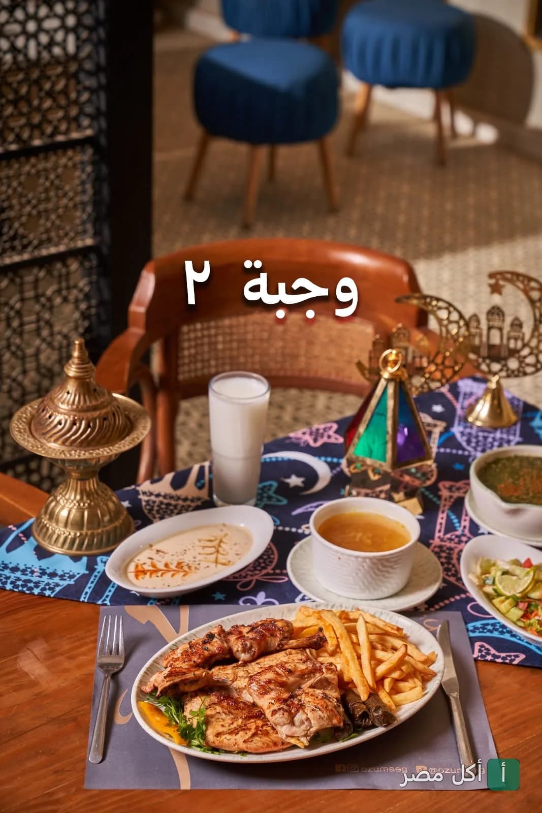وجبة إفطار رمضانية من مطعم عزومة تحتوي على دجاج مشوي وبطاطس مقلية مع ديكورات رمضانية.