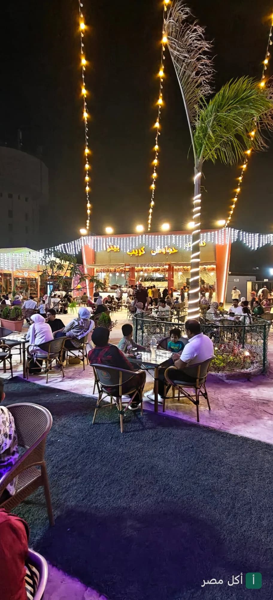 جلسات خارجية في مطعم رسلان بأطفيح ليلاً مع إضاءة ديكورية وأشجار نخيل.