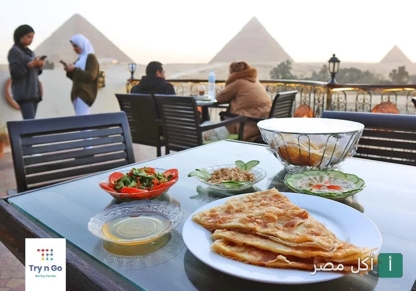 فطير مشلتت ومقبلات على طاولة في مطعم وكافيه الهضبة بنزلة السمان مع إطلالة مباشرة على أهرامات الجيزة.