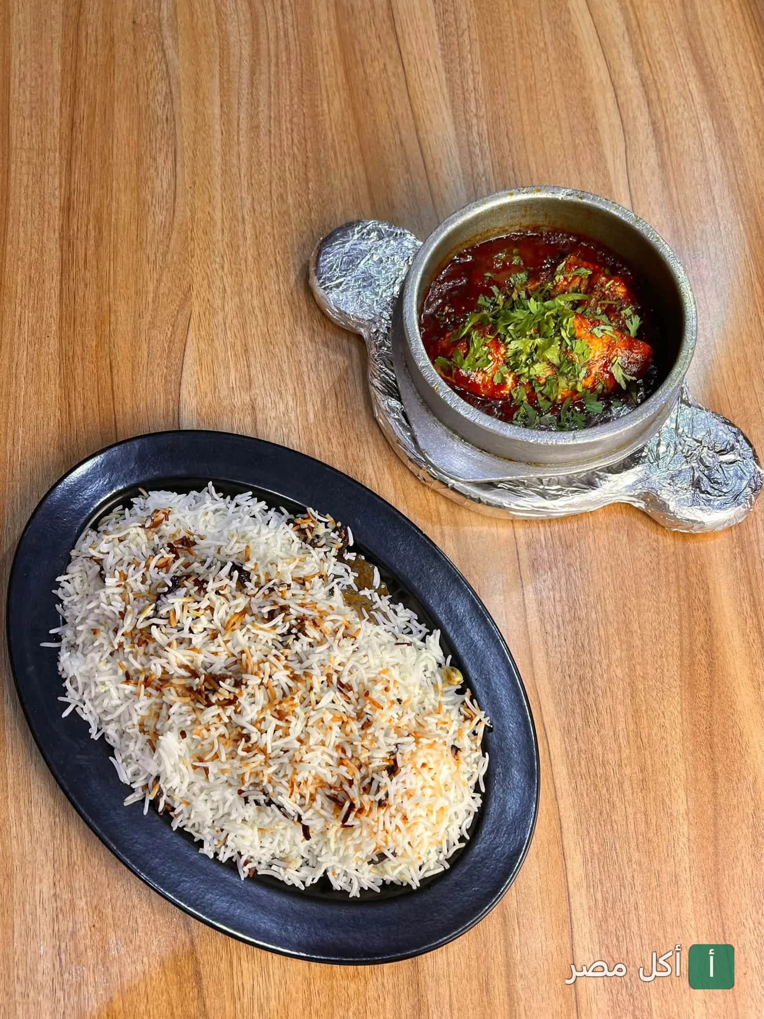 طبق أرز بسمتي بجانبه طاجن يمني ساخن في مطعم قصر الضيافة اليمنية بفيصل، الجيزة.