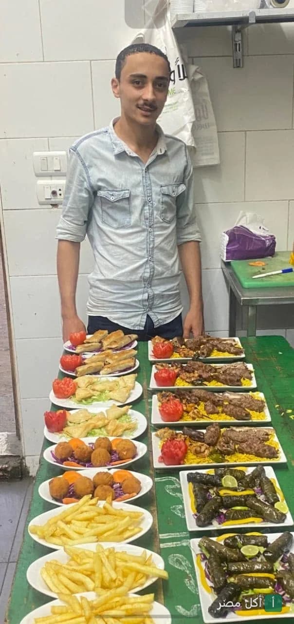 موظف في مطعم هالو بالجيزة يقف خلف طاولة مليئة بأطباق المشاوي والمقبلات والبطاطس المقلية.