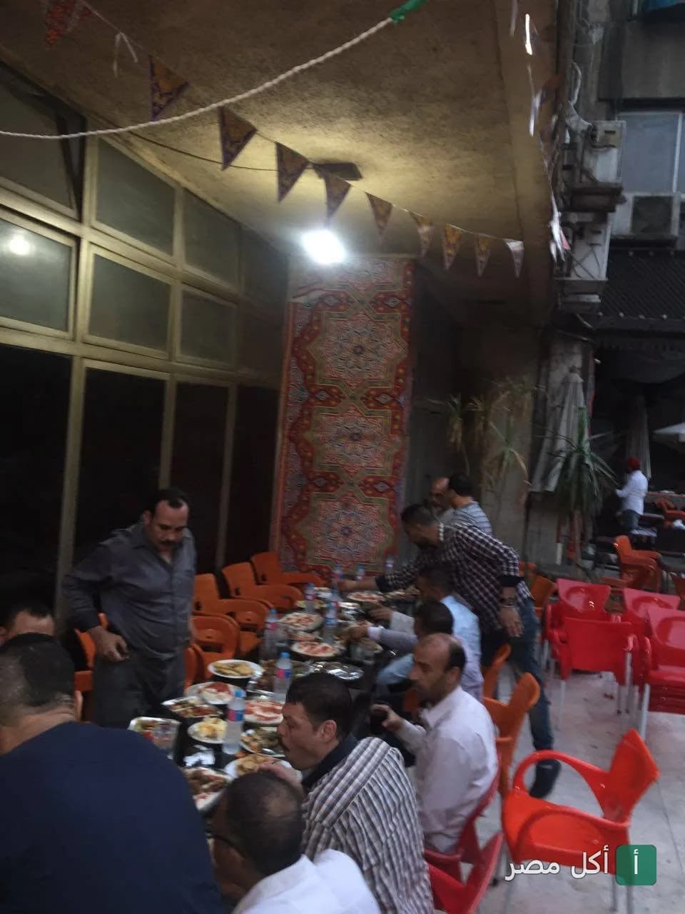 جلسة خارجية في مطعم وكافيه اركان بالدقي مع زبائن يتناولون الطعام على طاولات بلاستيكية حمراء.