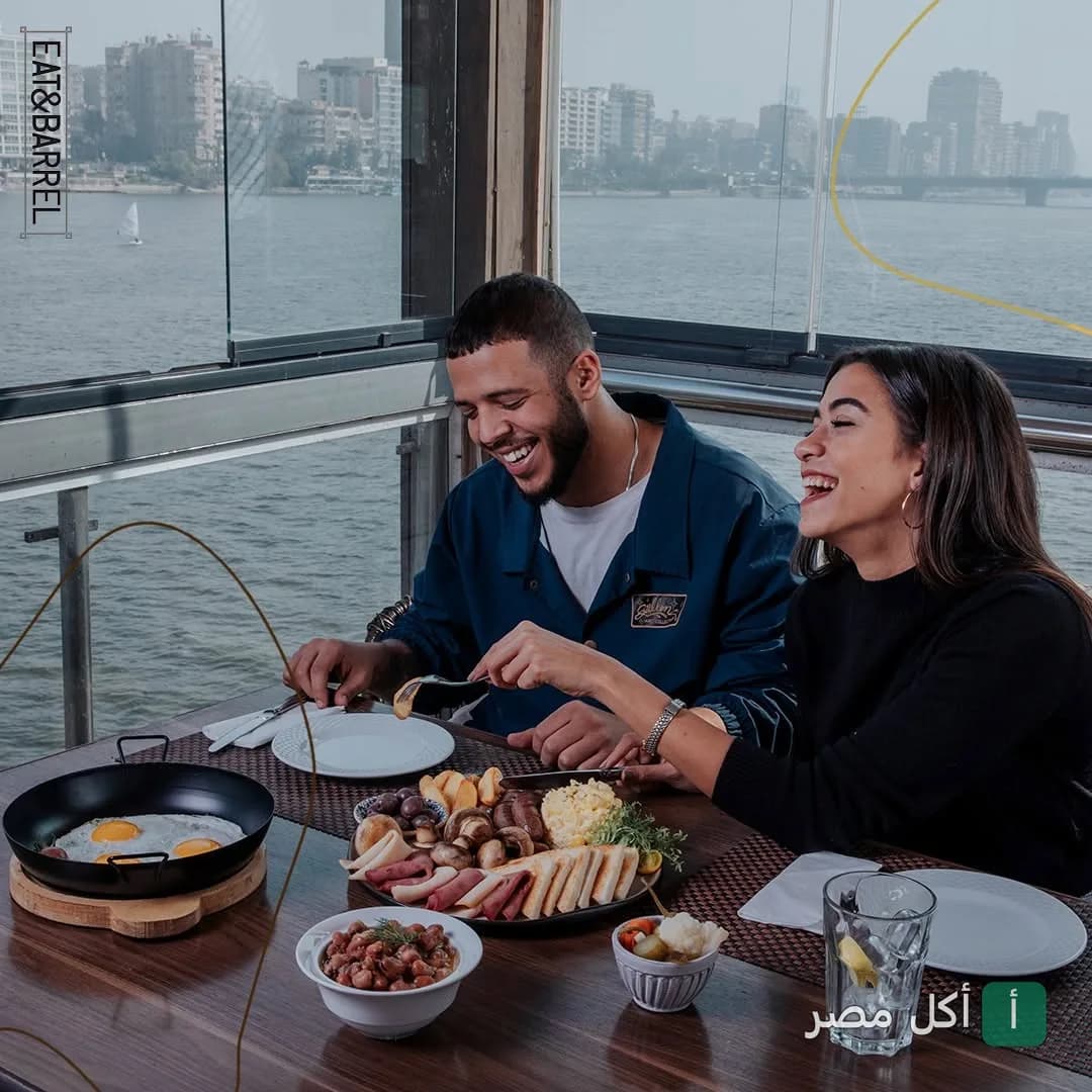 شاب وفتاة يضحكان أثناء تناول الإفطار في مطعم إيت آند باريل بالجيزة مع إطلالة مباشرة على النيل.