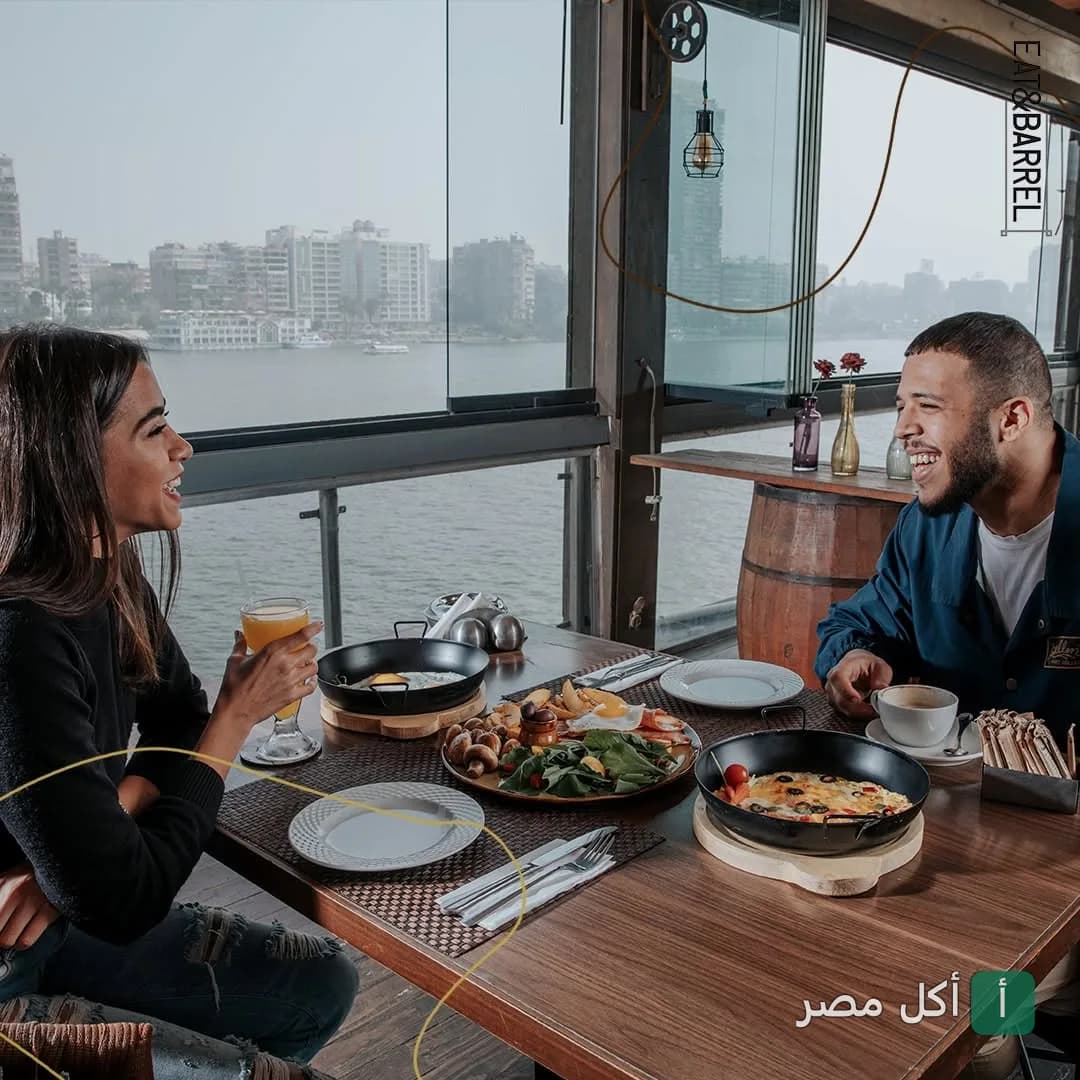 شخصان يتناولان الإفطار في مطعم إيت آند باريل بالجيزة مع إطلالة مباشرة على النيل.
