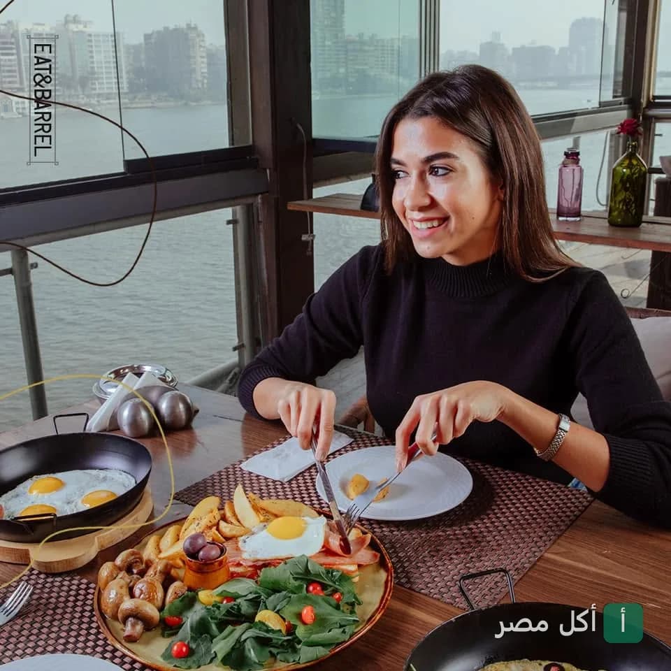 فتاة تتناول وجبة إفطار متنوعة في مطعم إيت آند باريل بالجيزة مع إطلالة على النيل.