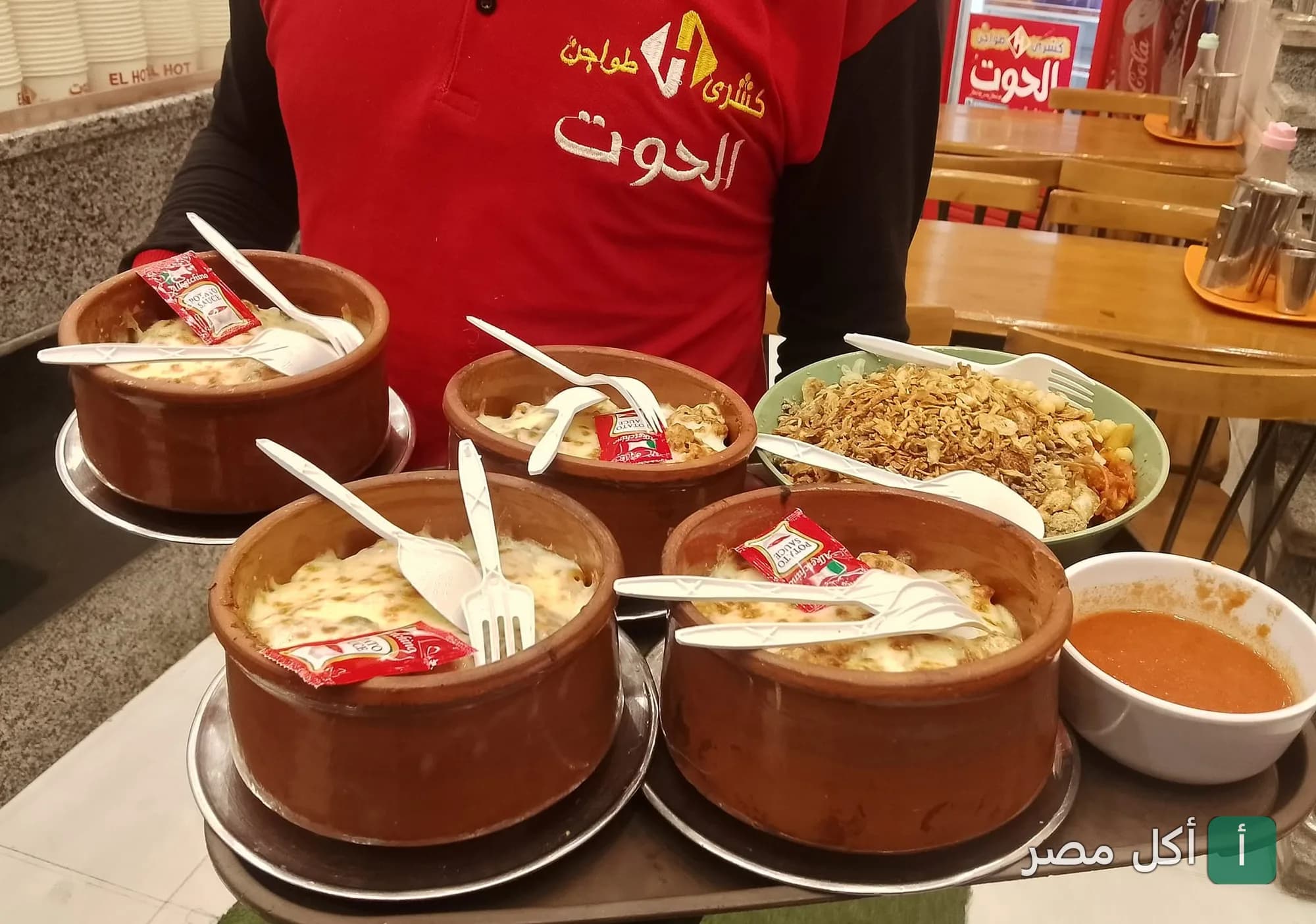 موظف في كشري الحوت بإمبابة يحمل صينية بها طواجن كشري ساخنة وأطباق جانبية.