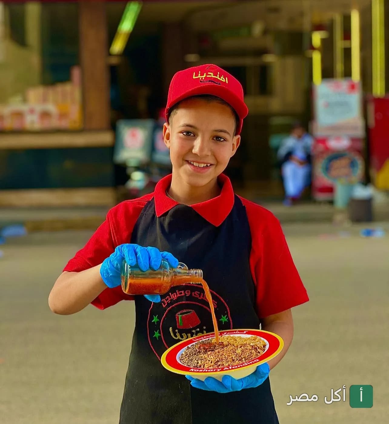 موظف في كشري افندينا يصب صلصة الطماطم على طبق كشري طازج في فرع القومية بإمبابة.