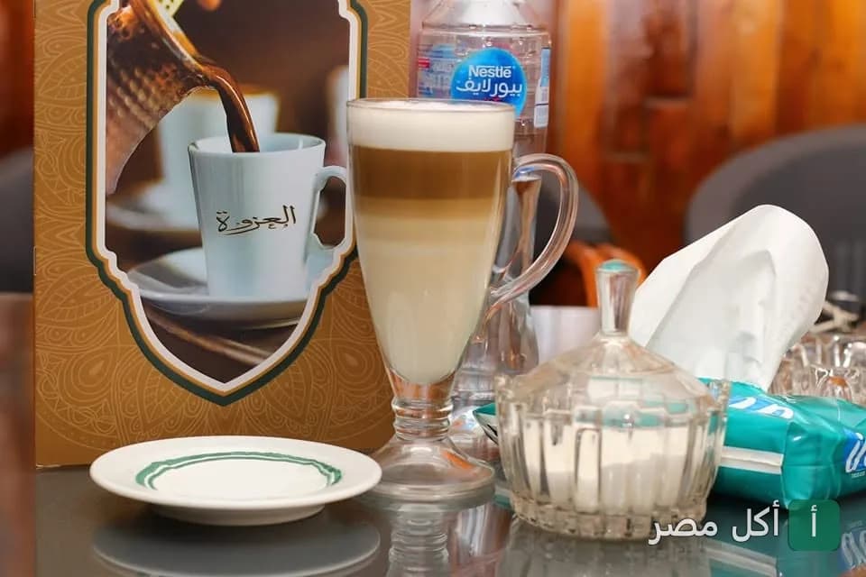 كوب لاتيه بطبقات في العزوة كافيه بإمبابة بجانب قائمة المشروبات.
