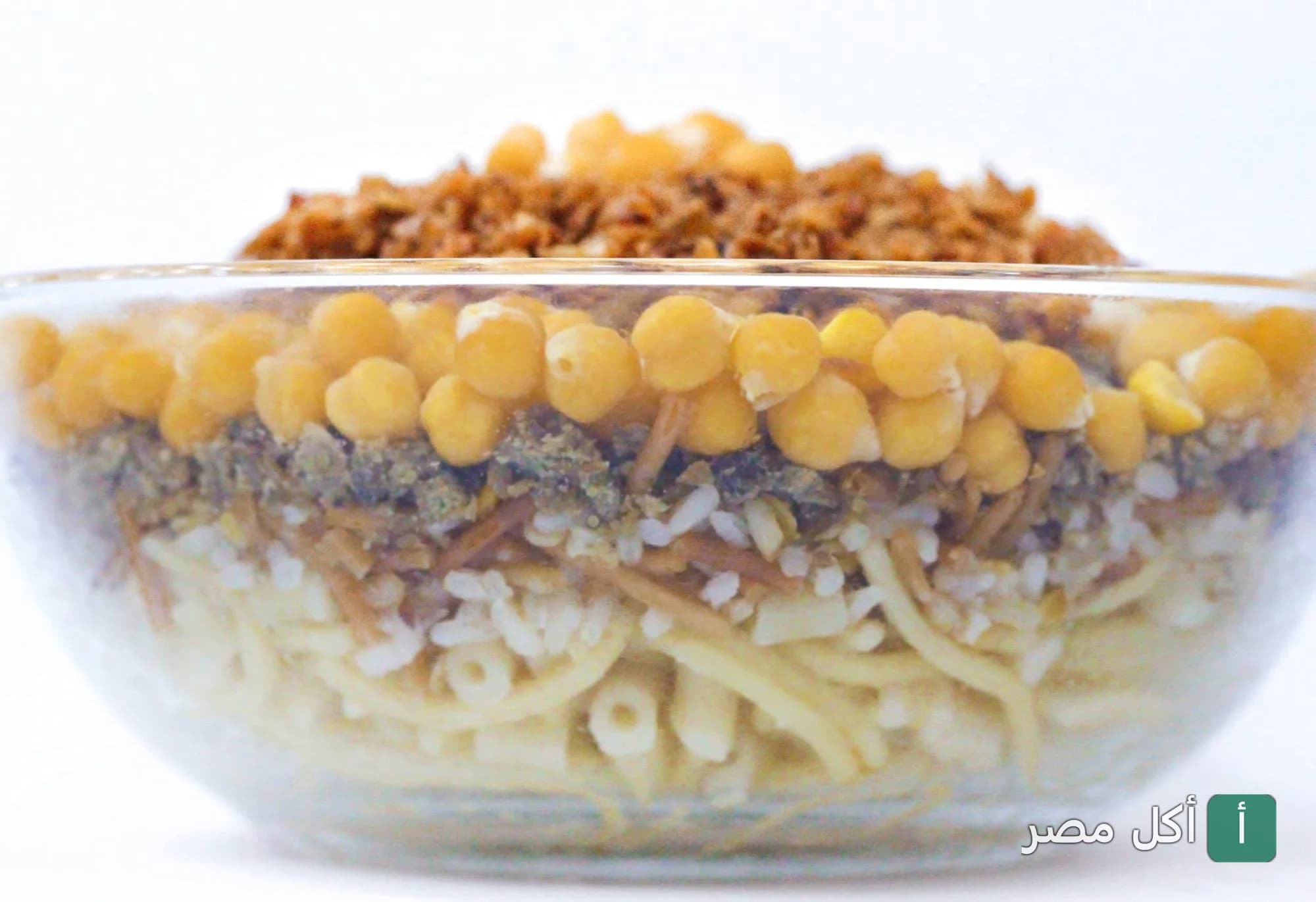 طبق كشري مصري في وعاء زجاجي شفاف يظهر طبقات الأرز والمكرونة والعدس والحمص والبصل المحمر من كشري الباشا بإمبابة.