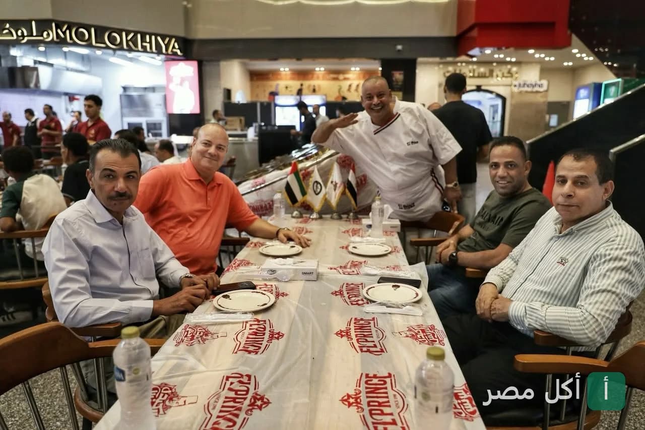 مجموعة من الزبائن يجلسون على طاولة طعام في مطعم البرنس، مع الشيف يحيى يرحب بالضيوف.