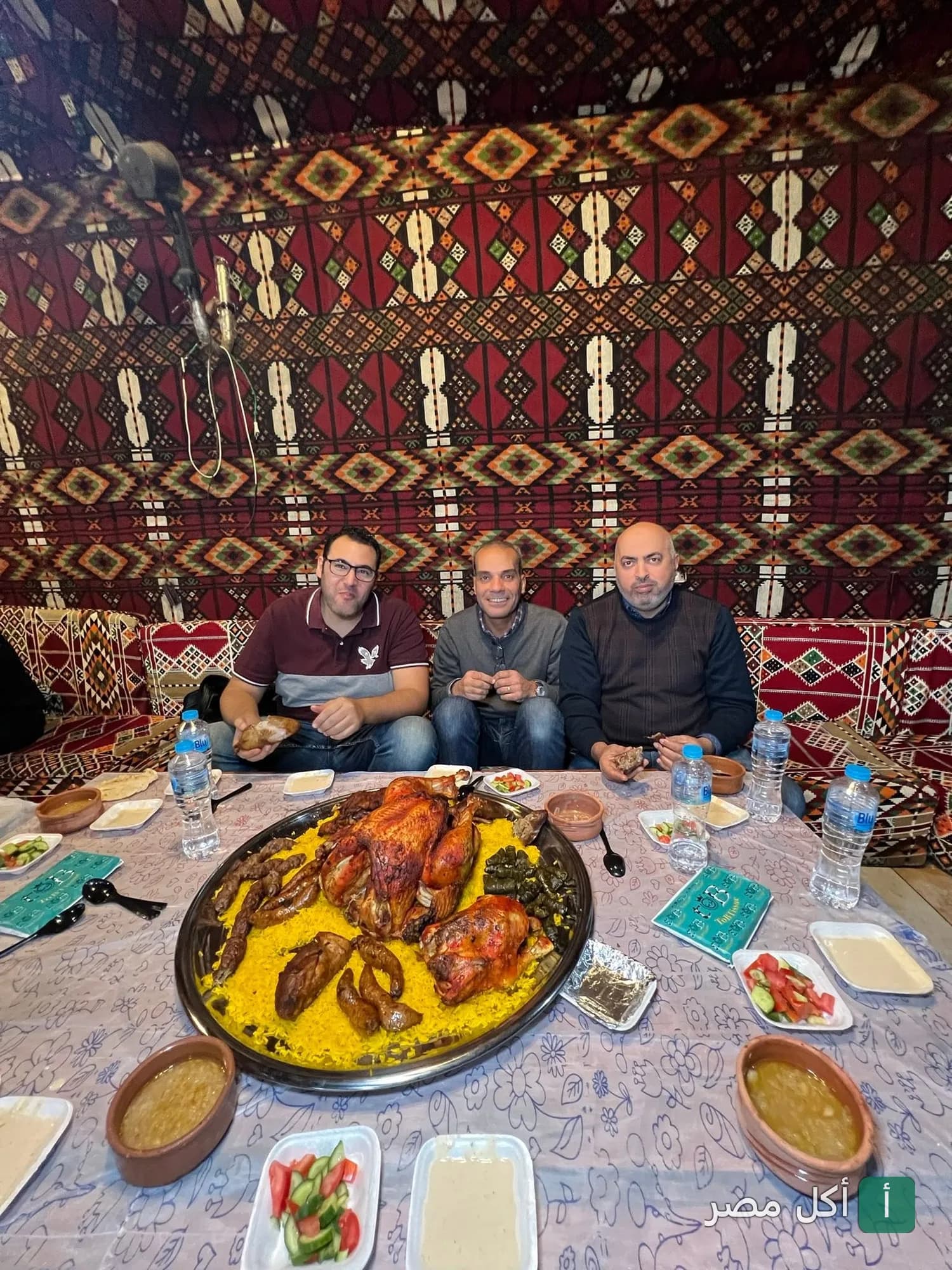 ثلاثة رجال يجلسون أمام صينية كبيرة من الأرز والدجاج المشوي في مطعم الشيخ محمد الكبدة الجملي بكرداسة.