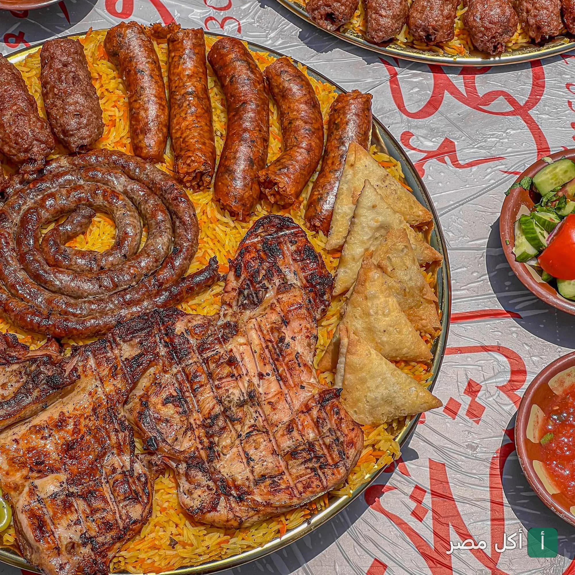 صينية مشويات مشكلة من مطعم الشيخ أبو عمر في الصف، تضم كفتة، سجق، ومشاوي على أرز أصفر مع سمبوسة.