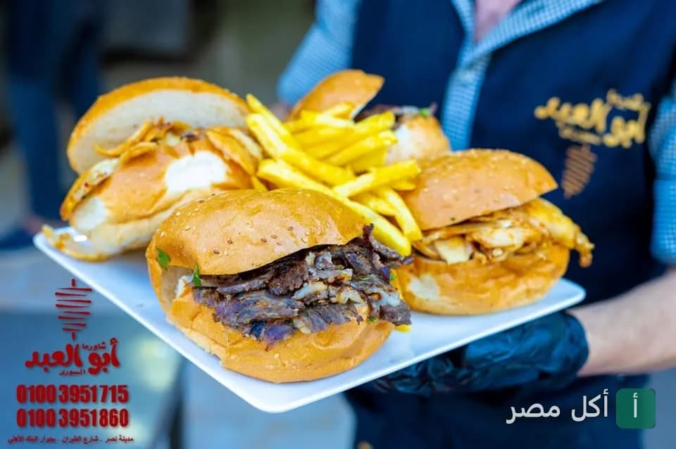عامل في مطعم شاورما أبو العبد السوري يحمل طبقاً يحتوي على ساندوتشات شاورما وبطاطس مقلية.