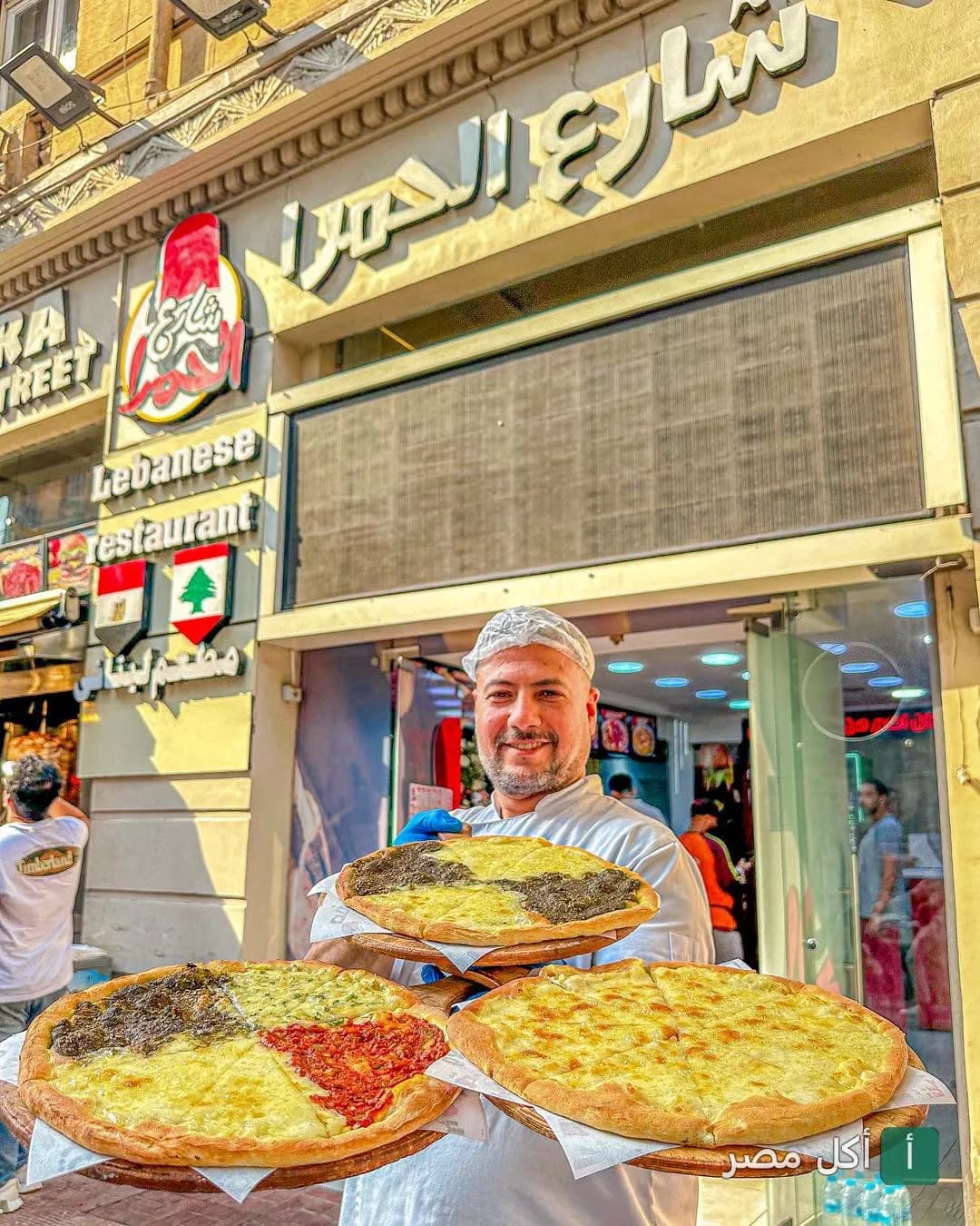 شيف مطعم شارع الحمراء في الشيخ زايد يحمل مناقيش طازجة أمام واجهة المطعم.