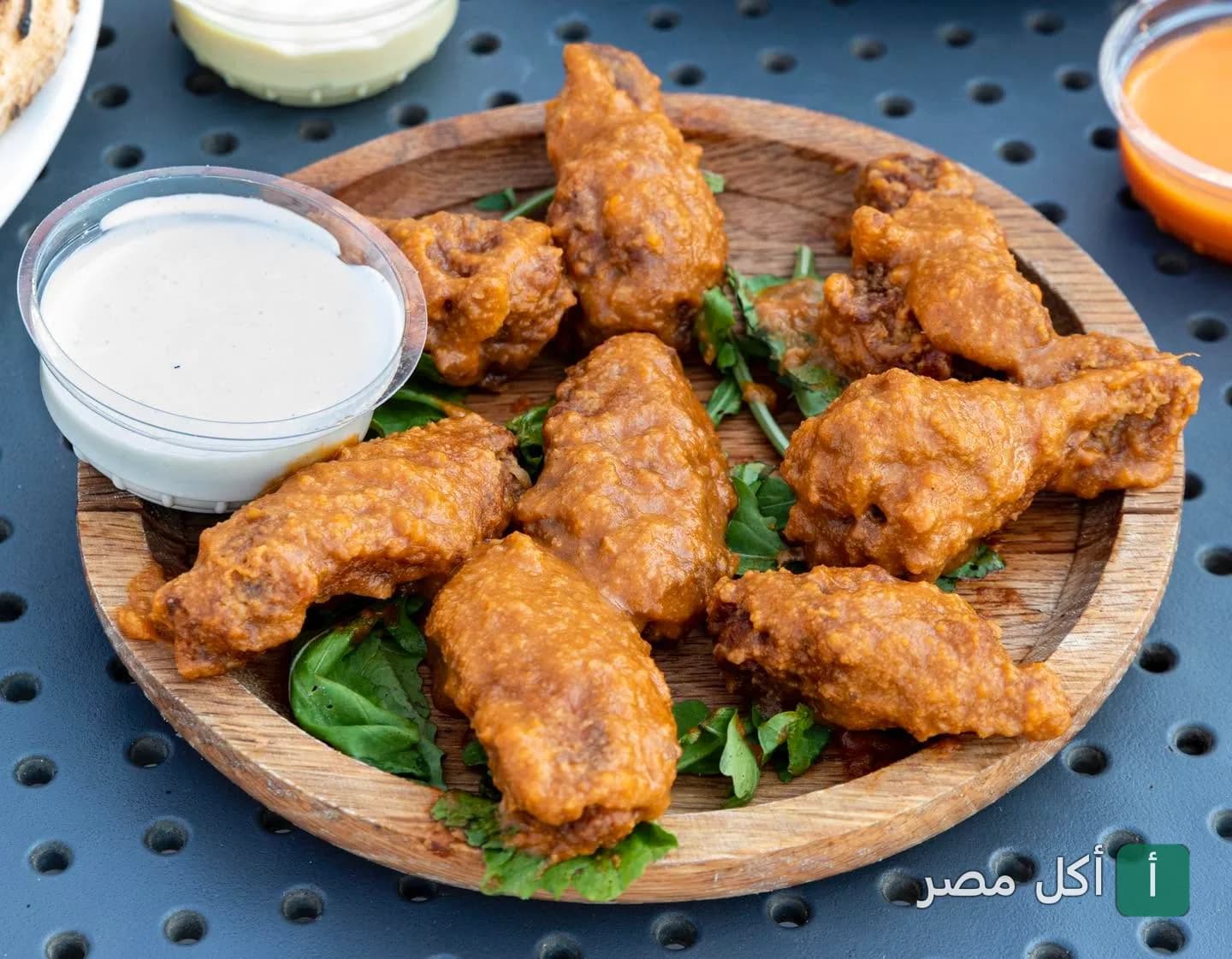 أجنحة دجاج بصوص حار تقدم على طبق خشبي مع صوص أبيض في مطعم Jimmy’s pizzeria بالشيخ زايد.