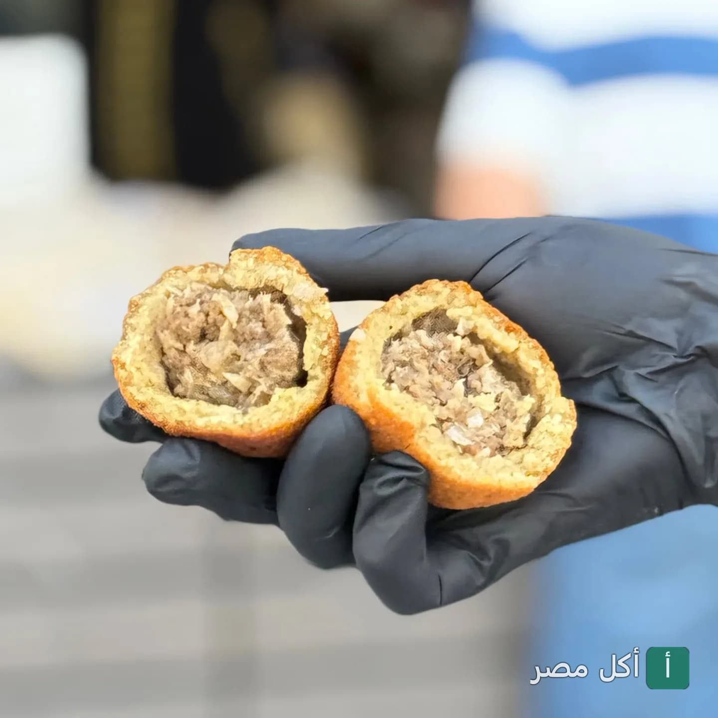 يد ترتدي قفاز أسود تمسك بقطعة كبة مقلية ومقسومة لنصفين تظهر حشوة اللحم في مطعم عروس الشام بالشيخ زايد.