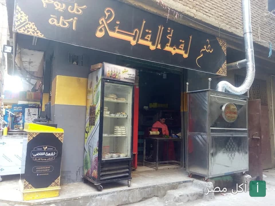 واجهة مطعم لقمة القاضي في الوراق مع لافتة المحل وثلاجة عرض ومعدات التحضير.