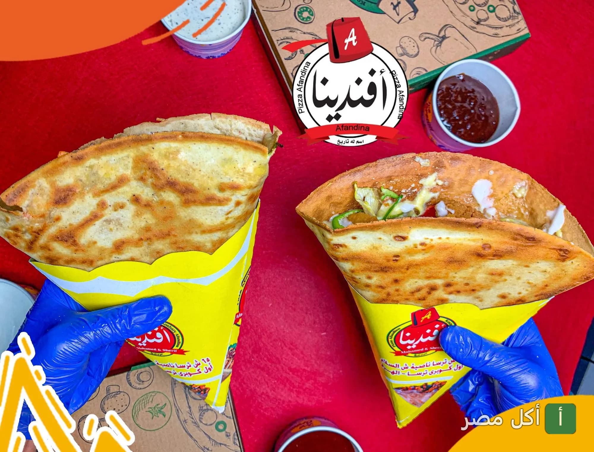 شخص يمسك ساندوتشات كريب من مطعم افندينا في حدائق الأهرام مع صوصات وعلبة بيتزا.