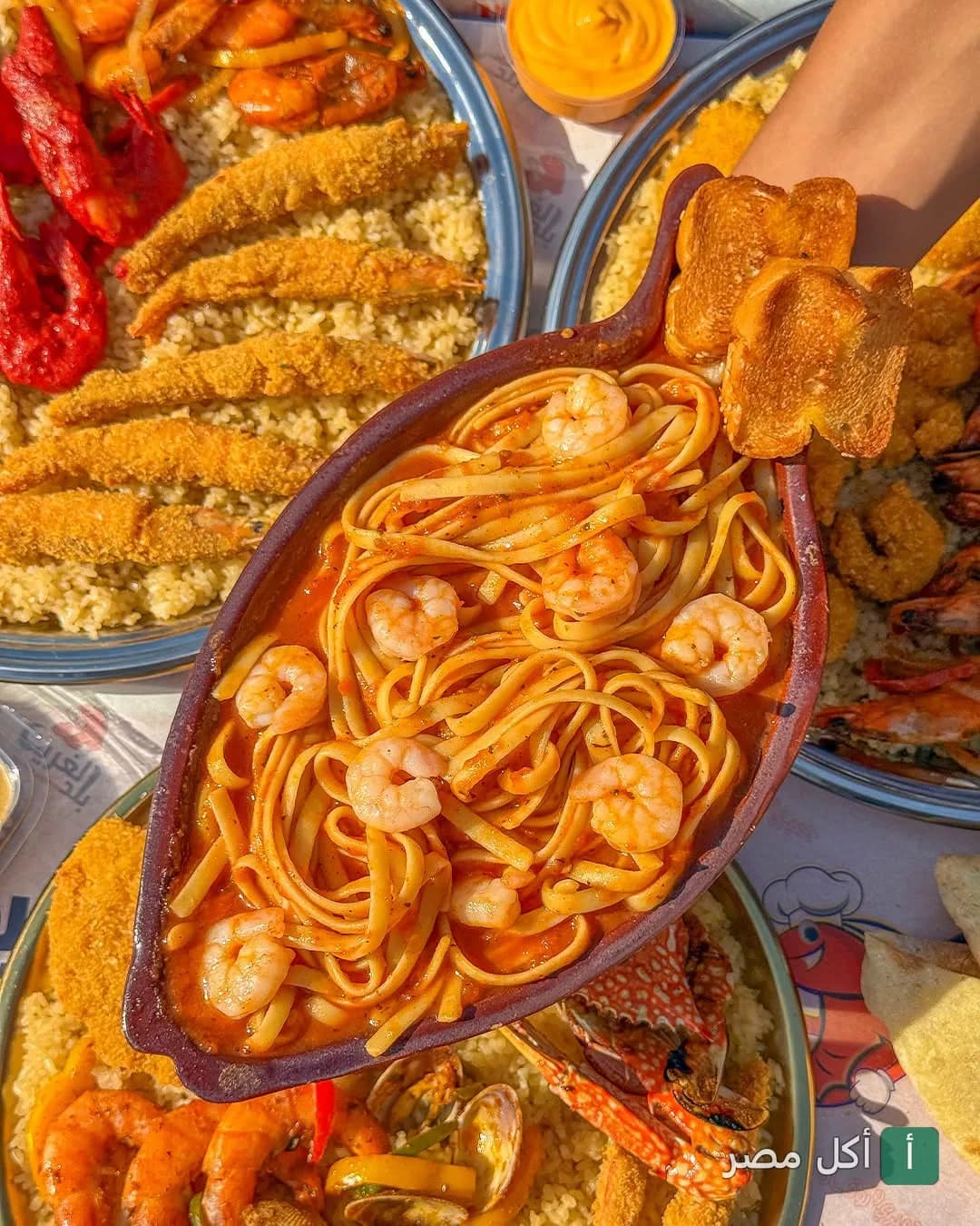 طبق مكرونة بالجمبري بصلصة حمراء في مطعم بلد الغريب بحدائق الأهرام، محاط بأطباق أرز ومأكولات بحرية متنوعة.