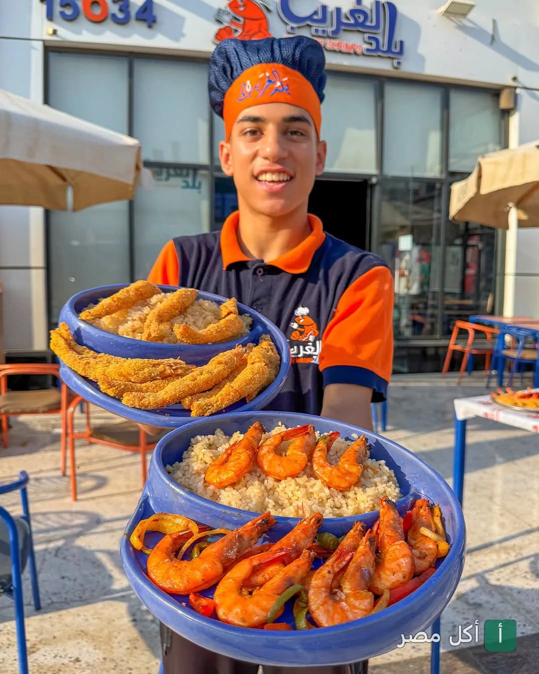 موظف مطعم بلد الغريب في حدائق الأهرام يقدم أطباق الجمبري والأرز أمام واجهة المطعم.
