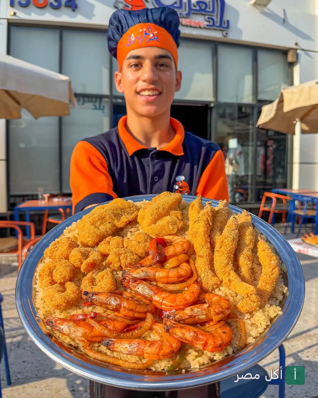 موظف مطعم بلد الغريب بحدائق الأهرام يقدم طبق كبير من المأكولات البحرية المقلية والمشوية مع الأرز.