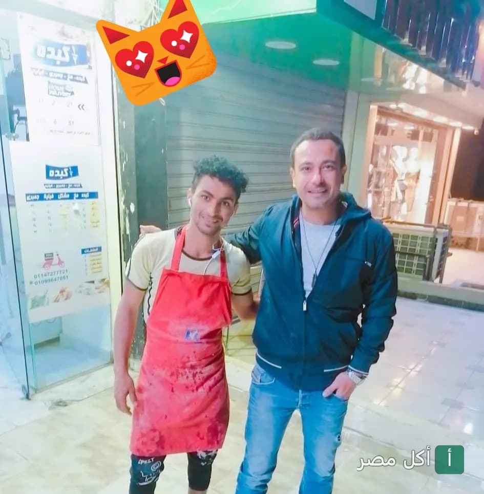 موظف بزي العمل الأحمر يقف أمام واجهة مطعم نص كبده في الأهرام بالجيزة.