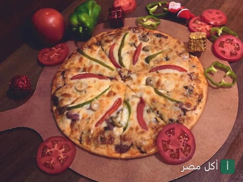 بيتزا مطعم أكيلز بالأهرام مزينة بشرائح الطماطم والفلفل الأخضر على لوح تقديم خشبي.