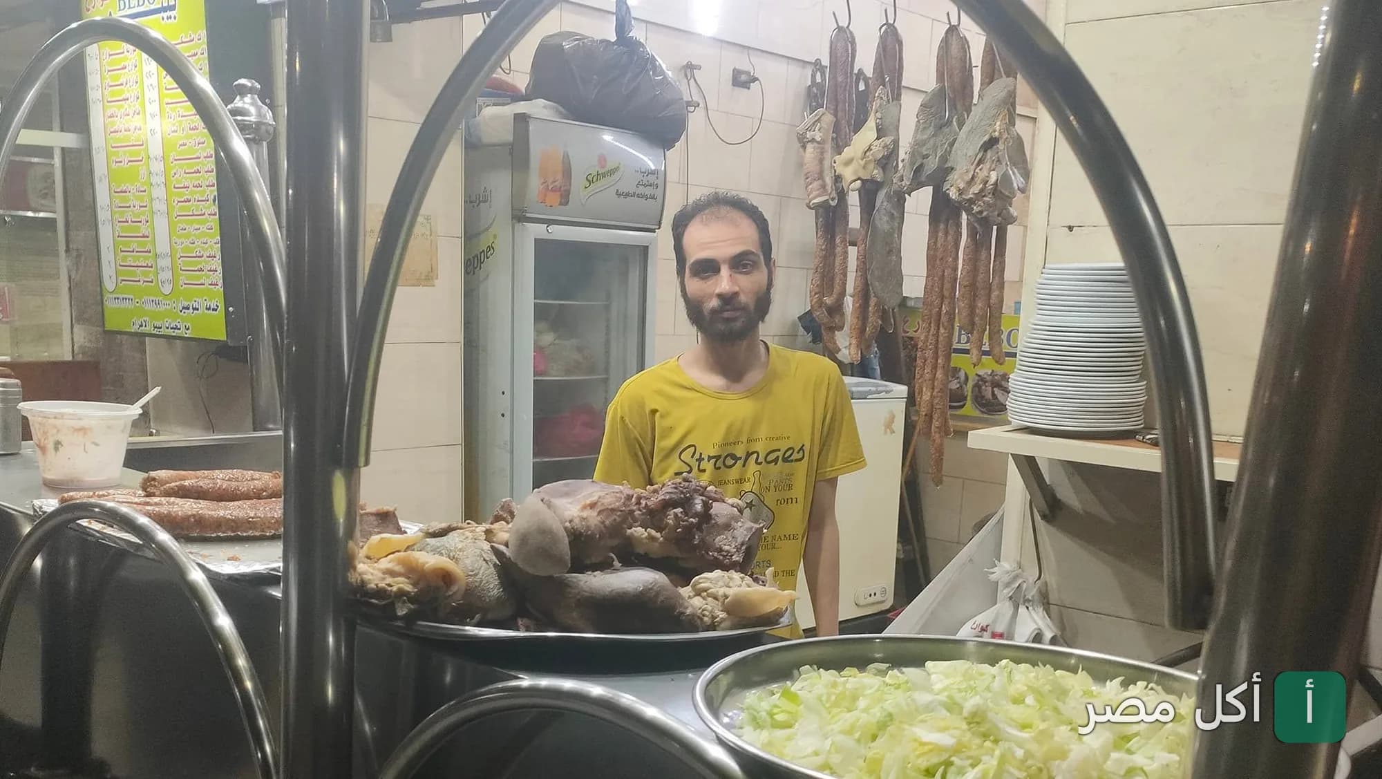 طباخ في مسمط بيبو بالهرم يقف أمام أطباق متنوعة من المشاوي والأكلات الشرقية.